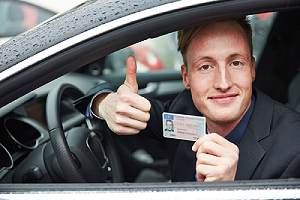Man in a car holding driver's license. Driving without a license may seem self-explanatory