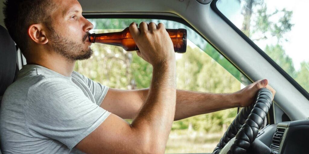 man holds alcohol in his hand while driving violates traffic rule