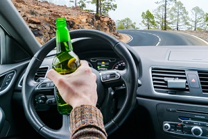 young man driving a car on the road with a bottle of beer