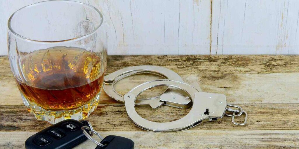 whiskey in a glass on w wooden table with handcuffs and car keys