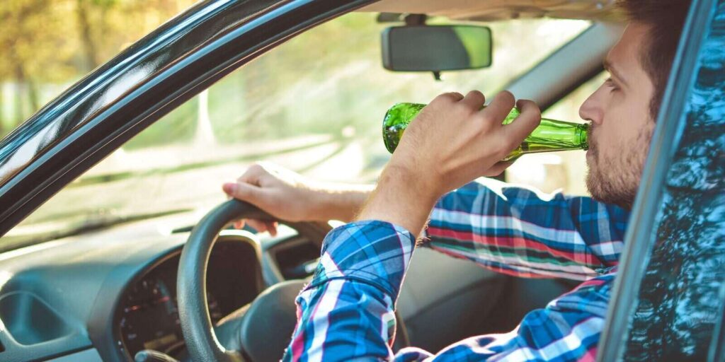 man driving a car with a bottle of beer