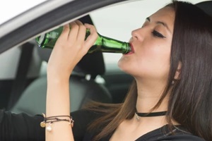 closeup young woman sitting in car holding green beer bottle and drinking